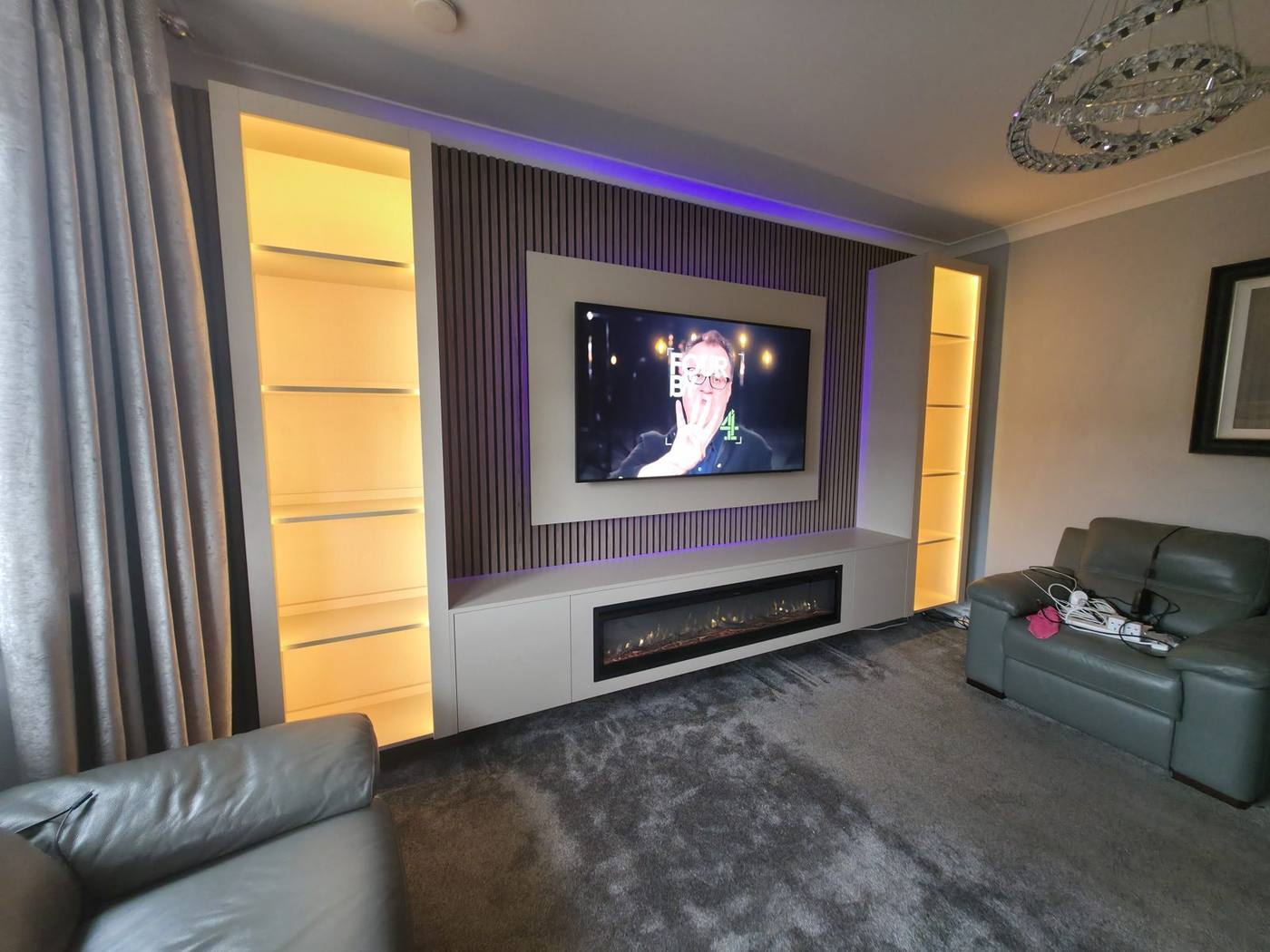 Walnut slat media wall with amber-lit shelving and linear electric fire